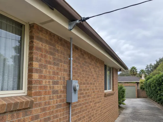 Overhead service cable and point-of-attachment bracket on a brick house exterior in Cherrybrook